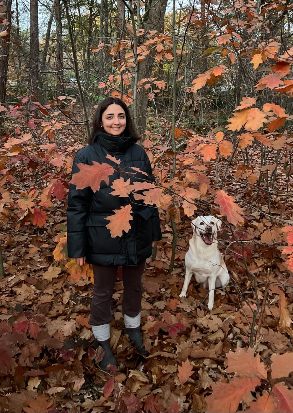 Negin standing among autumn oak leaves in a forest with her dog